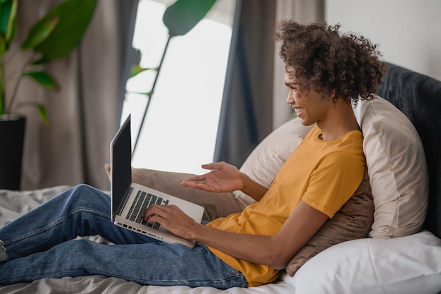 Curlyhaired young guy sitting on a bed with a laptop