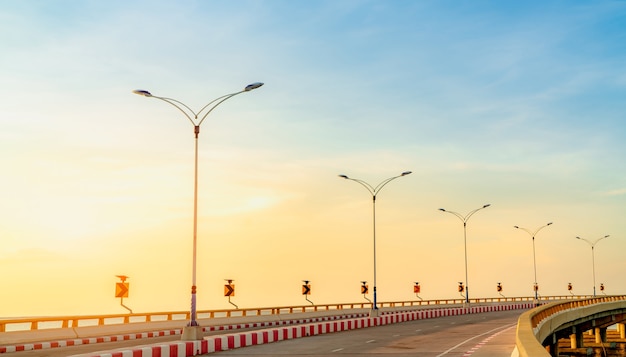 Curve concrete road with curve and footpath traffic sign beside the sea at sunset time. Solar panel energy on yellow curve traffic sign. Road trip on summer vacation. Red and white traffic sign.