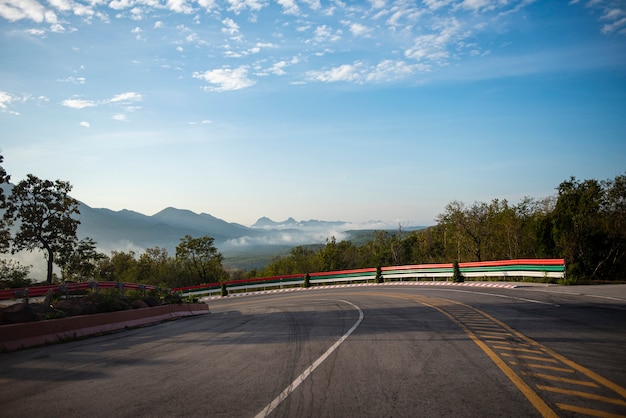 Curve road driving a car on mountain road downhill. Dramatic curve beautiful blue sky cloud with mist fog in the morning.