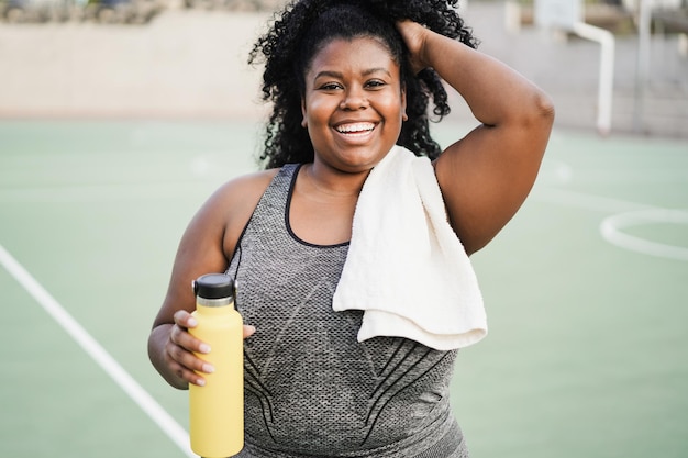 Curvy african woman smiling at camera while doing running routine in park city  Focus on face