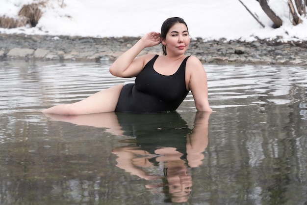 Curvy plus size young model in black bathing suit lying in geothermal water in outdoors pool at spa