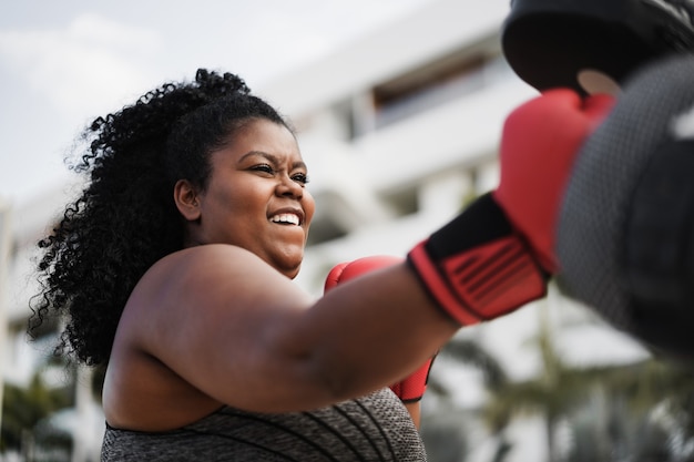 Curvy woman and personal trainer doing boxing workout session outdoor - Focus on face