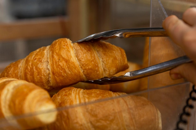 The customer picks up a fresh croissant on the counter with metal tongs Traditional pastries for breakfast and coffee Closeup