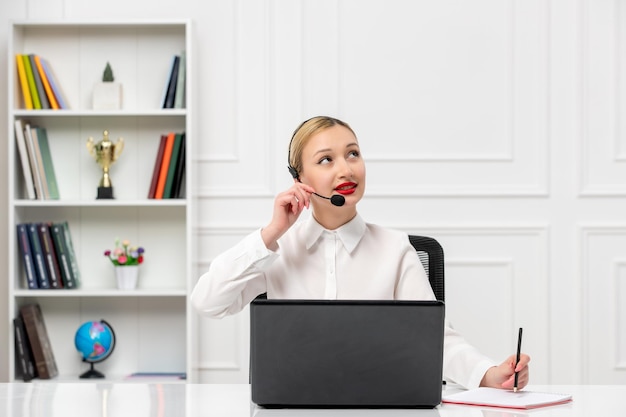 Customer service cute blonde girl in office shirt with headset and computer looking up and thinkin