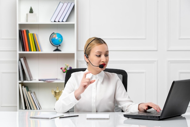 Customer service pretty blonde girl in white shirt with laptop and headset talking to a client