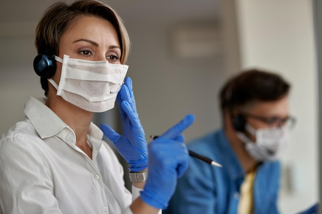 Customer service representative wearing protective face mask while using headset and talking with her clients during virus epidemic