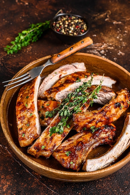 Cut BBQ grilled pork rack spareribs in a wooden plate. Dark background. Top view.