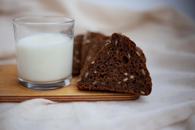 Cut black bread into pieces on a wooden cutting board next to a glass of fresh milk