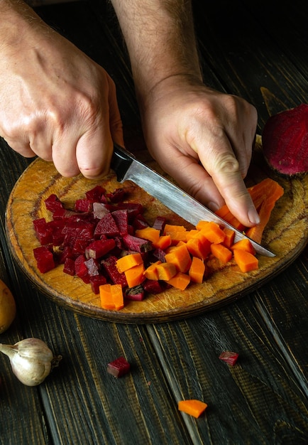 Cut the boiled carrots and beets into small pieces to prepare the vinaigrette Knife in the chef hand Vegetable dish concept or Ukrainian national cuisine