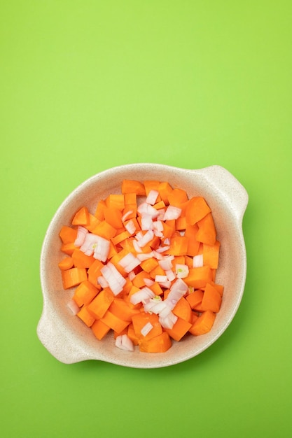 Cut cubes of fresh carrot in the bowl on green