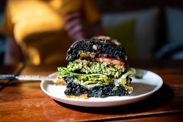 Cut half of Broccoli quinoa charcoal burger topped with guacamole, mango salsa and fresh salad served on a white plate. Creative vegan meal for vegetarians.