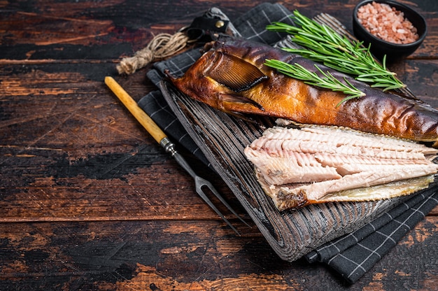 Cut Hot smoked fish  on a wooden board with rosemary. Dark wooden background. Top view. Copy space.