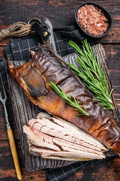 Cut Hot smoked fish  on a wooden board with rosemary. Dark wooden background. Top view.