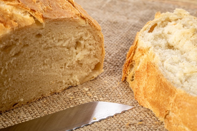 A cut loaf of white Ukrainian bread and a kitchen knife on a burlap napkin bread crumbs are scattered on the tableclose up