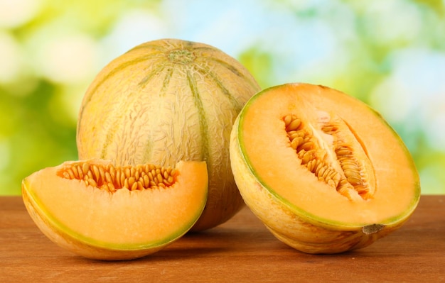 Cut melon on wooden table on green background