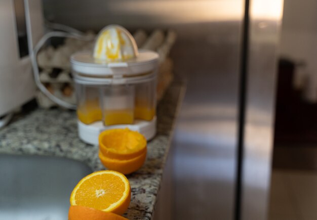 Cut orange halves by electric squeezer with juice inside on kitchen counter Healthy drink concept