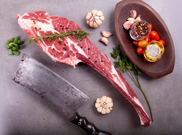 Cut of raw short rib meat marbled with fat and bone on stone with spices and cleaver