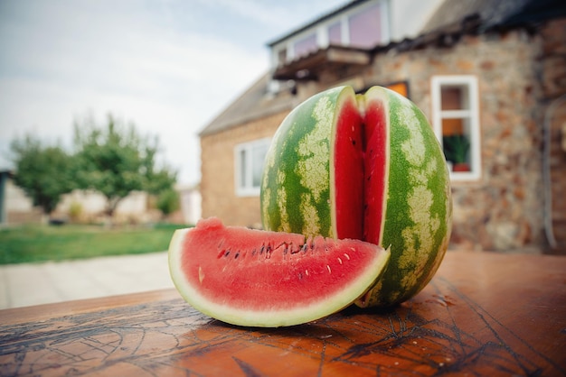 Cut ripe juicy watermelon on a wooden table against the background of a private house in summer