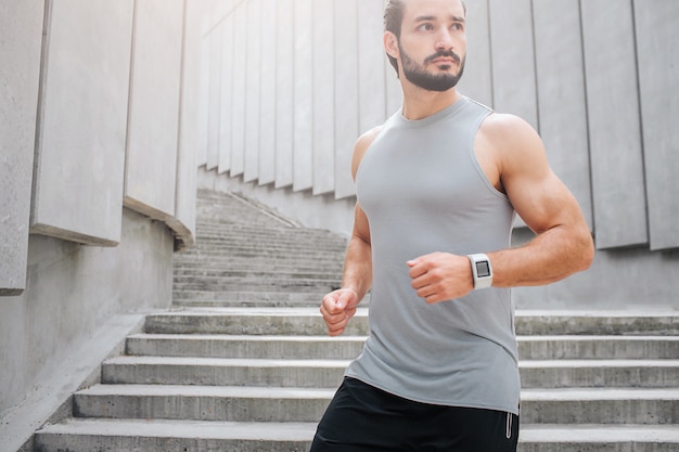 Cut view of young man jogging. He looks to right. Guy has handband. He looks confident calm and concentrated.