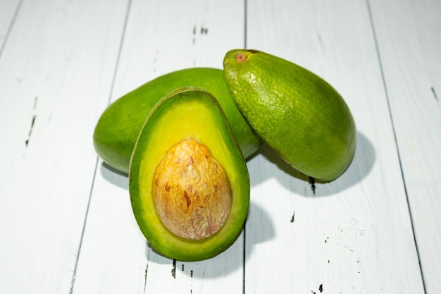 Cut and whole avocado on a white wooden background