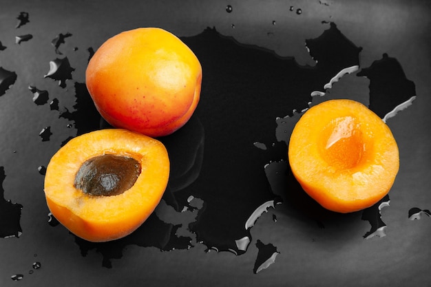 Cut and whole wet apricots on a wet dark background Fresh juicy ruddy apricots on a dark