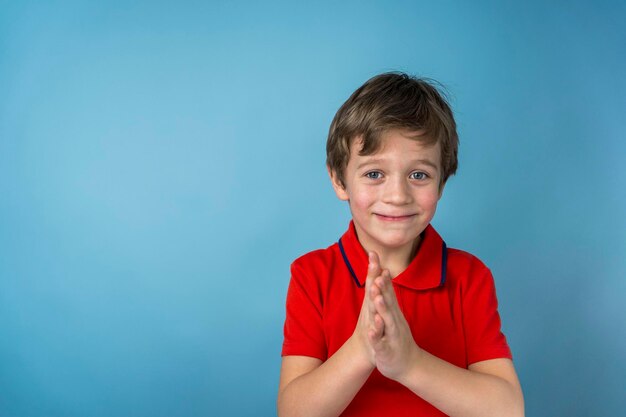 A cute 5-year-old Caucasian boy in a red T-shirt rubs hand in hand and smiles slyly. The boy is happy with the result