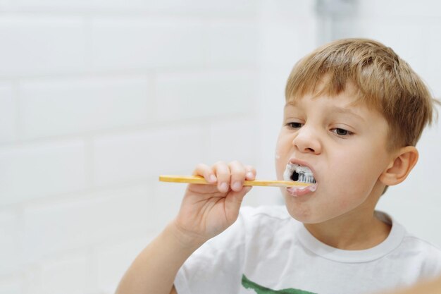 Cute 5 years old boy brushing teeth with bamboo tooth brush in bathroom Image with selective focus