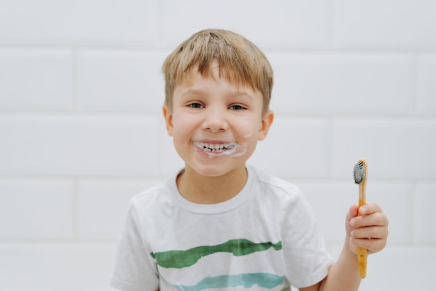 Cute 5 years old boy brushing teeth with bamboo tooth brush in bathroom Image with selective focus