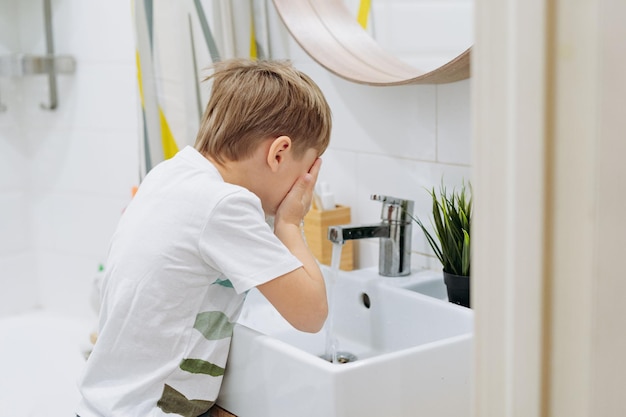 Cute 6 years old boy washing his face over the sink in bathroom Image with selective focus