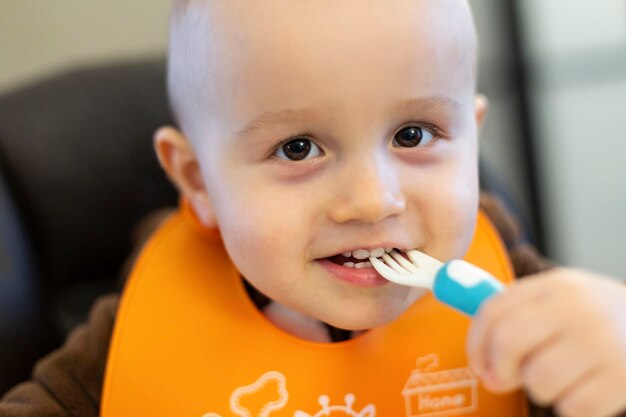 Cute adorable baby of 18 monts old taking plastic fork in his mouth and playing with food