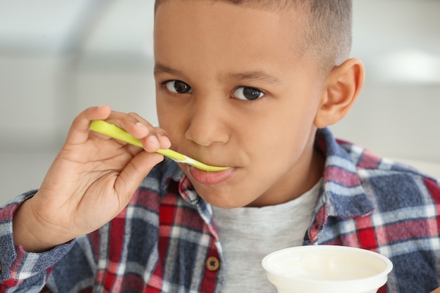 Cute African American boy eating yogurt at home, closeup