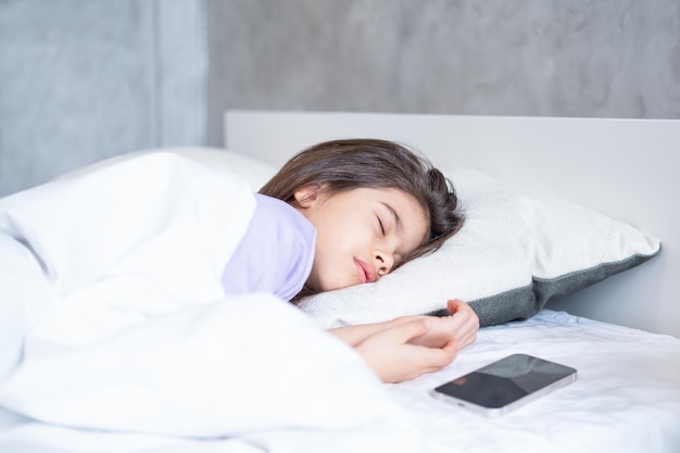 cute arab child girl with long hair sleeping on white bedding at home phone are near her