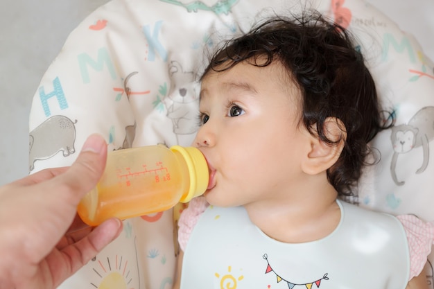 A cute Asian baby drinking orange juice from mother hand holding the bottle