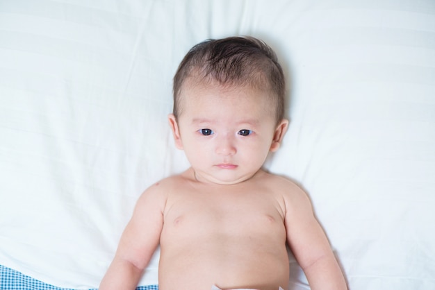 Cute Asian baby lying on a white pillow, on bed