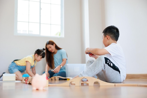 Cute asian boy playing wood block building rail way and road on the floor and his mother and sister help him to do that at home