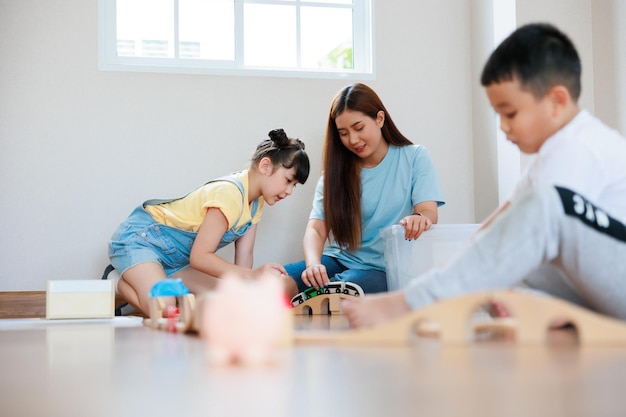 Cute asian boy playing wood block building rail way and road on the floor and his mother and sister help him to do that at home