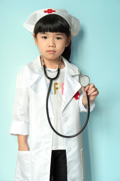 Cute asian child in doctor coat with stethoscope on color background