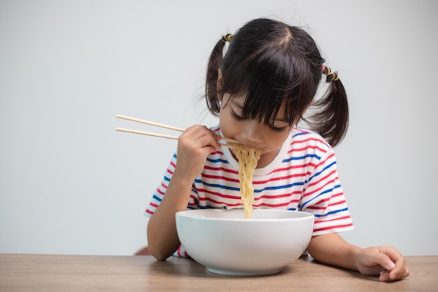 Cute Asian child girl eating delicious instant noodles at home