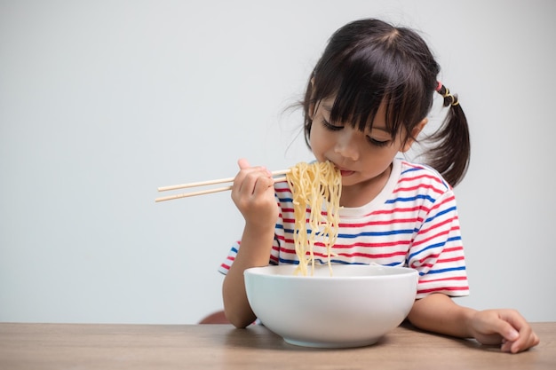 Cute Asian child girl eating delicious instant noodles at home