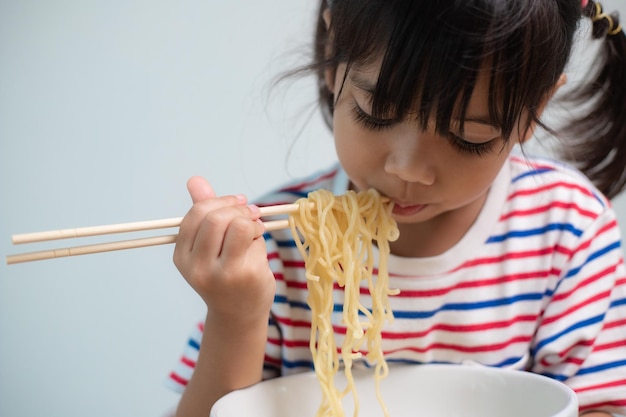 Cute Asian child girl eating delicious instant noodles at home