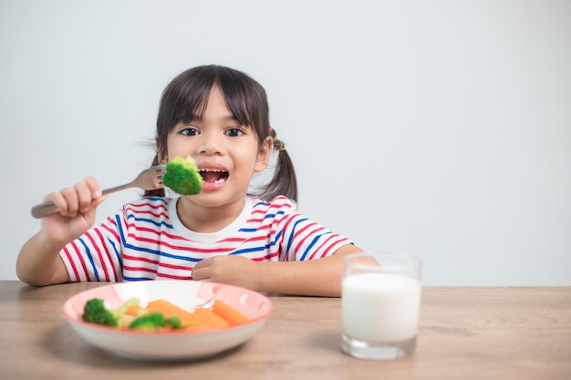 Cute asian child girl eating healthy vegetables and milk for her meal