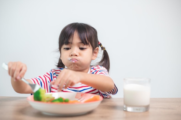 Cute asian child girl eating healthy vegetables and milk for her meal