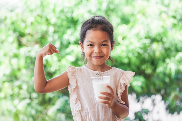 Cute asian child girl holding glass of milk and make strong gesture 