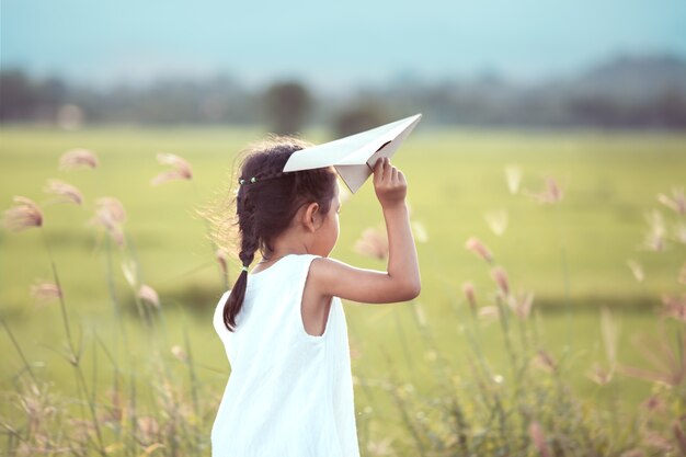 Cute asian child girl playing toy paper airplane in the field in vintage color tone