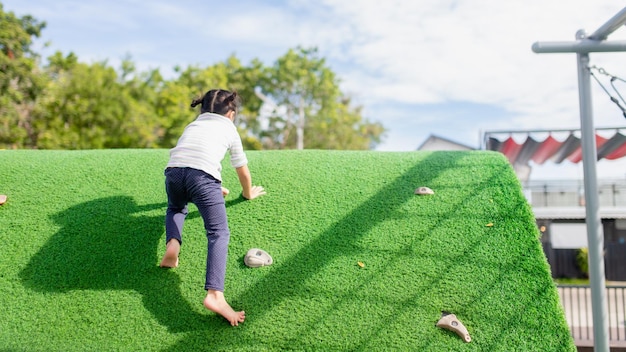 Cute Asian girl having fun trying to climb on artificial boulders at schoolyard playground Little girl climbing up the rock wall Hand Eye Coordination Skills development