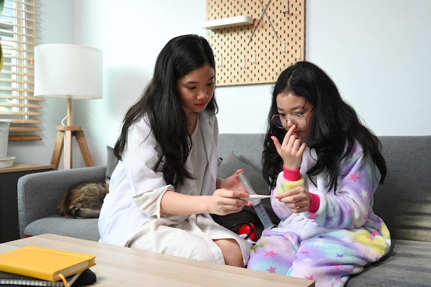 Cute asian girl medical uniform playing as doctor with her young sister at home