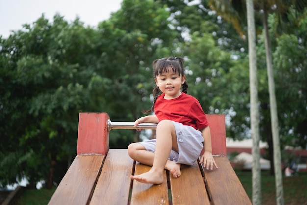 Cute asian girl play on school or kindergarten yard or playground Healthy summer activity for children Little asian girl climbing outdoors at playground Child playing on outdoor playground