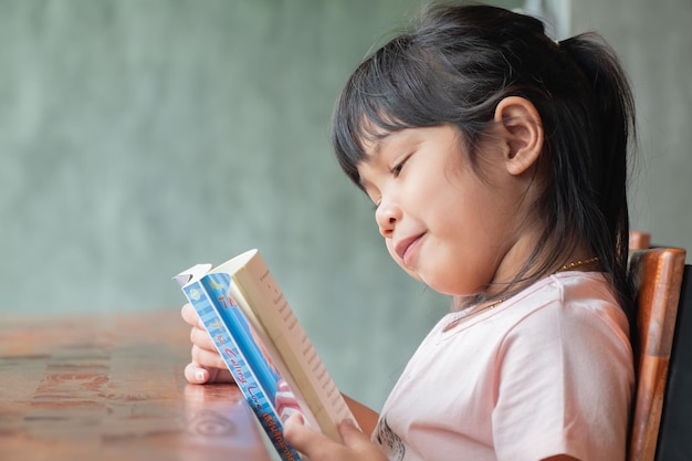 Cute asian girl reading a book sitting on a wooden tablehappy life cocept