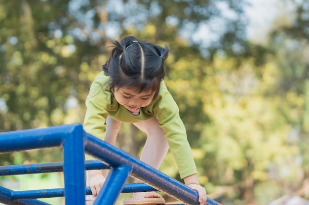 Cute asian girl smile play climb the bar on school or kindergarten yard or playground Healthy activity children Little girl climbing outdoors at playground Child playing on outdoor playground