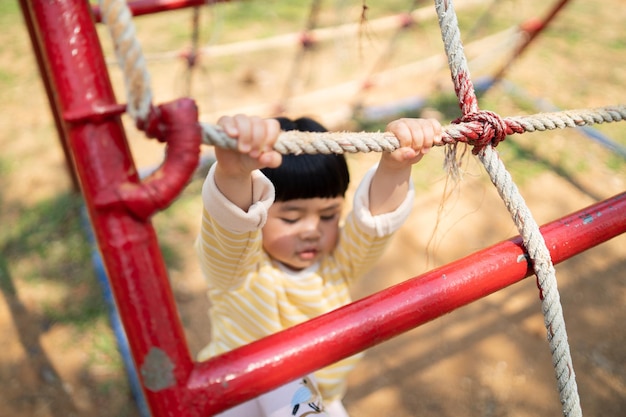 Cute asian girl smile play on school or kindergarten yard or playground Healthy summer activity for children Little asian girl climbing outdoors at playground Child playing on outdoor playground